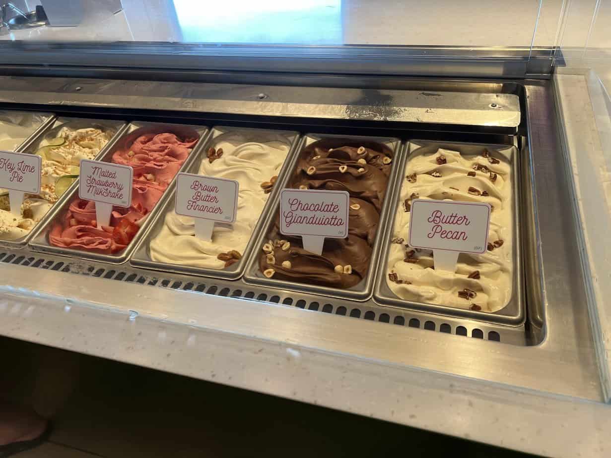 Scoops of colorful ice cream in cups at Lick Me Till Ice Cream parlor.